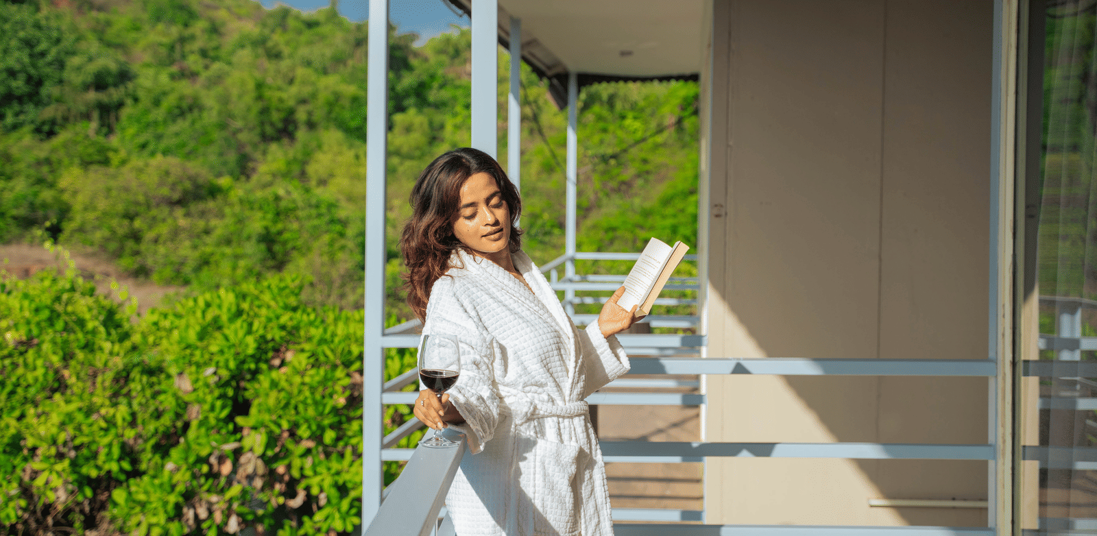 A woman enjoying the morning sunlight on a balcony while holding a book - Perfectstayz Koko Maya